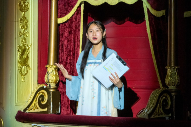 A young person performing, lit up in the box of a theatre