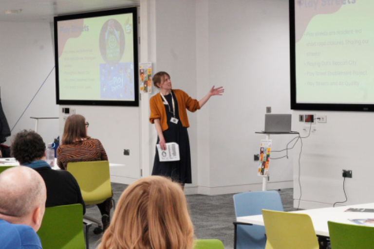 A presenter talking to an audience with a PowerPoint