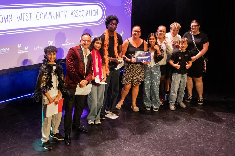 Members of Moortown West Community Association posing on stage with an award certificate during a youth awards ceremony.