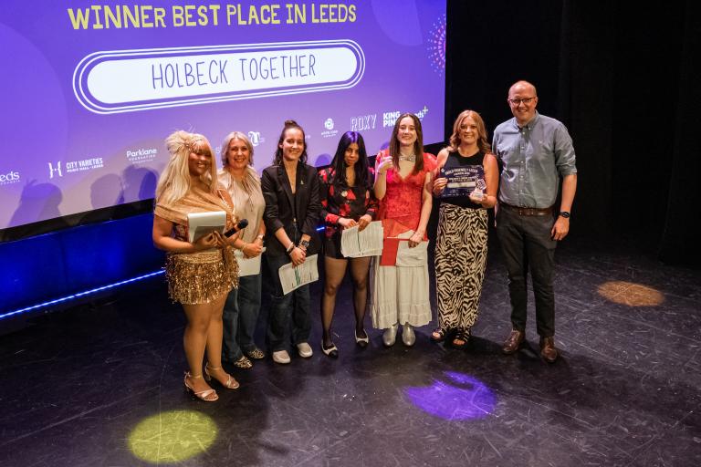 Representatives from Holbeck Together pose on stage with a certificate and trophy after winning the "Best Place in Leeds" award.