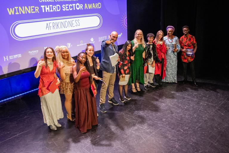 Representatives from Afrikindness pose on stage with an award plaque after winning the Overall Contribution Third Sector Award.