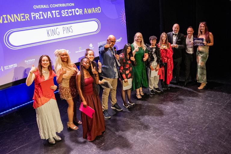 Representatives from King Pins pose on stage with a trophy and award plaque after winning the Overall Contribution Private Sector Award.